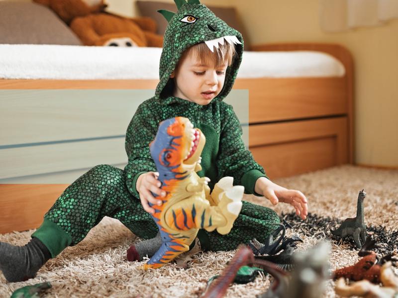 En dreng i dinosaurkostume leger med dinosaurfigurer på gulvet. 